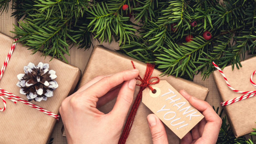 Ruce zdobí stylový vánoční dárek v lněné látce s větví červené bobule