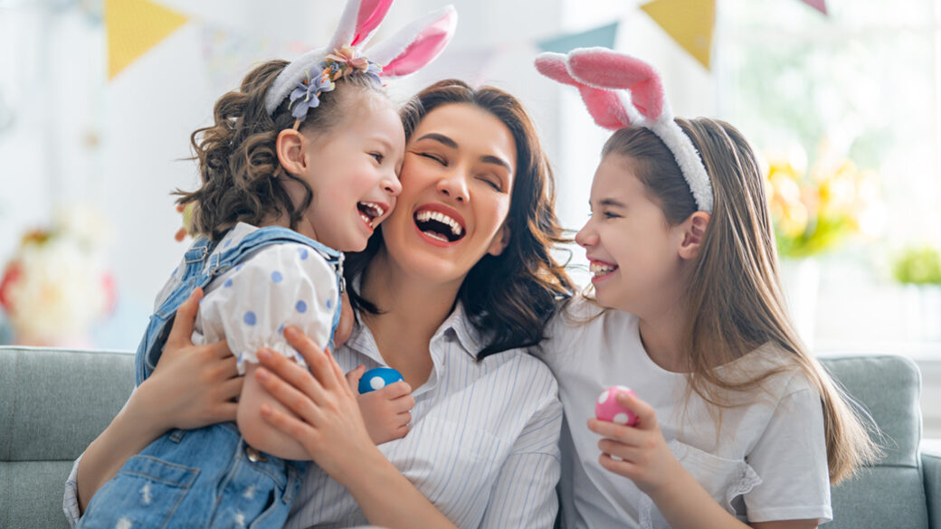 Smiling mom and two daughters enjoying while decorating easter eggs