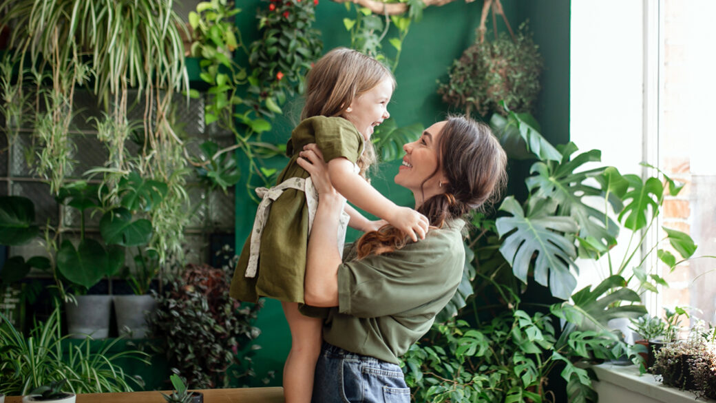Matka a dcera vysazují zelené rostliny ve skleníku.