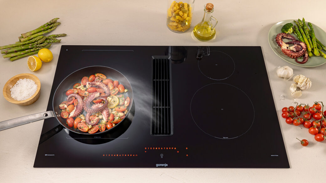 Gorenje G800 series hood-in-hob with built-in extraction vent removing steam and odours while cooking octopus and vegetables, surrounded by fresh ingredients on a modern kitchen counter.