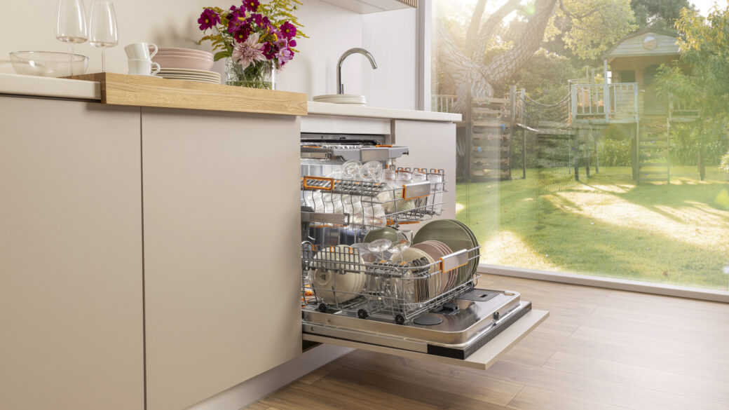 A modern dishwasher loaded with dishes in a bright summer kitchen interior.